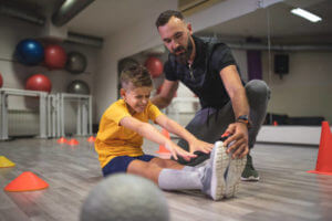 Strong and healthy father and a personal trainer, teaching and training his son at a gym.