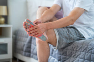 A man is sitting on his bed, experiencing pain in his leg and foot due to plantar fasciitis.