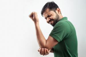 A person with an elbow injury is experiencing pain, causing them to grimace.